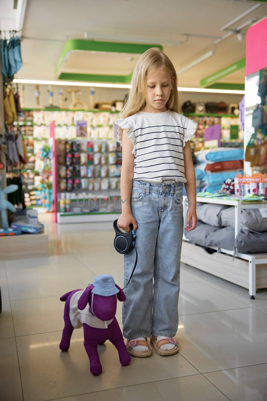 Portrait of sad little girl with toy dog on leash dreaming about real pet animal standing over pet store background