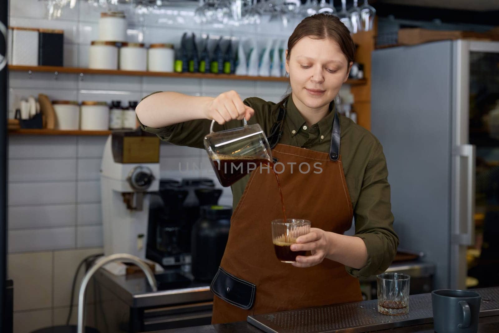 Woman barista pouring transparent brown aroma coffee drink in cup from glass jug. Process of high quality aromatic beverage preparation