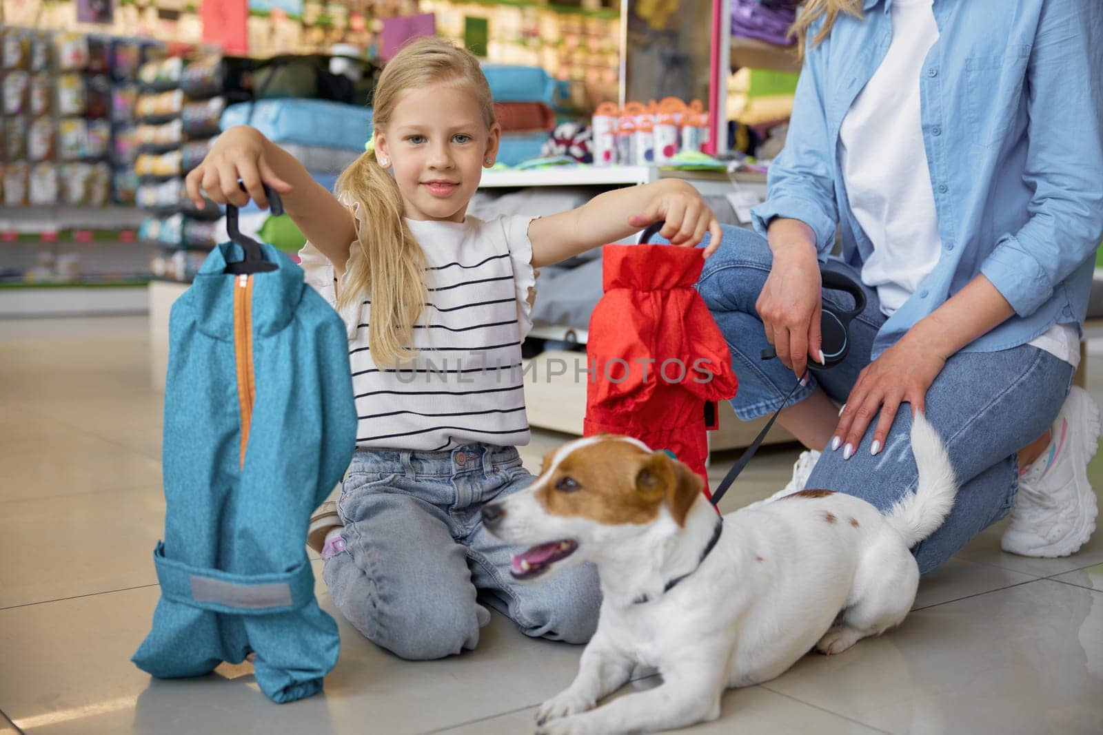 Portrait of little girl showing new comfort winter clothes for dog during shopping with mother at pet store