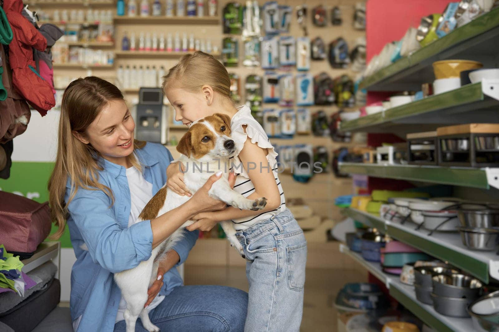 Mother helping cute little girl posing with dogs in hands over pet shop background. Happy time together and family shopping enjoyment
