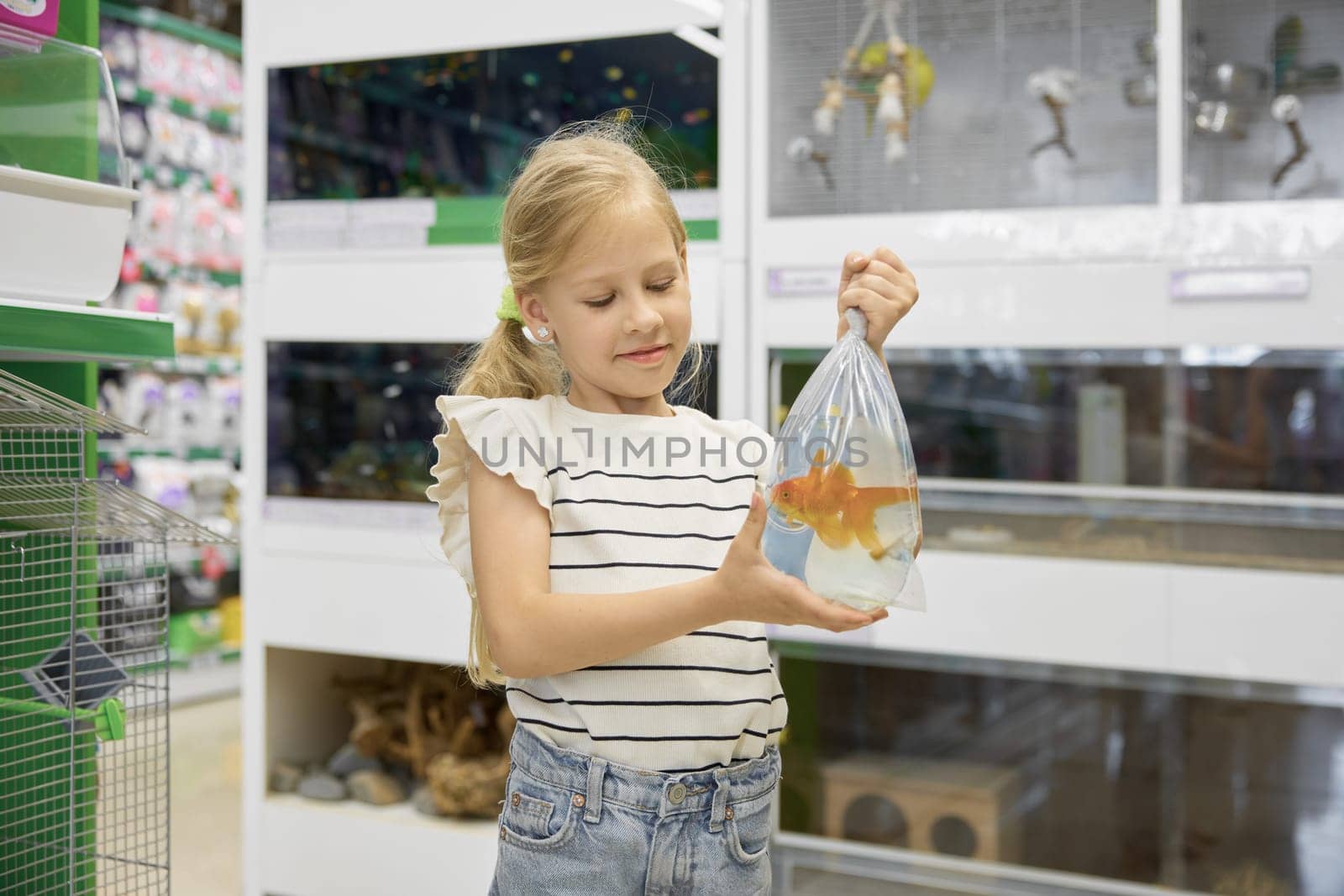 Portrait of cute smiling little girl holding packet with new gold fish pet standing over supermarket vet department store background