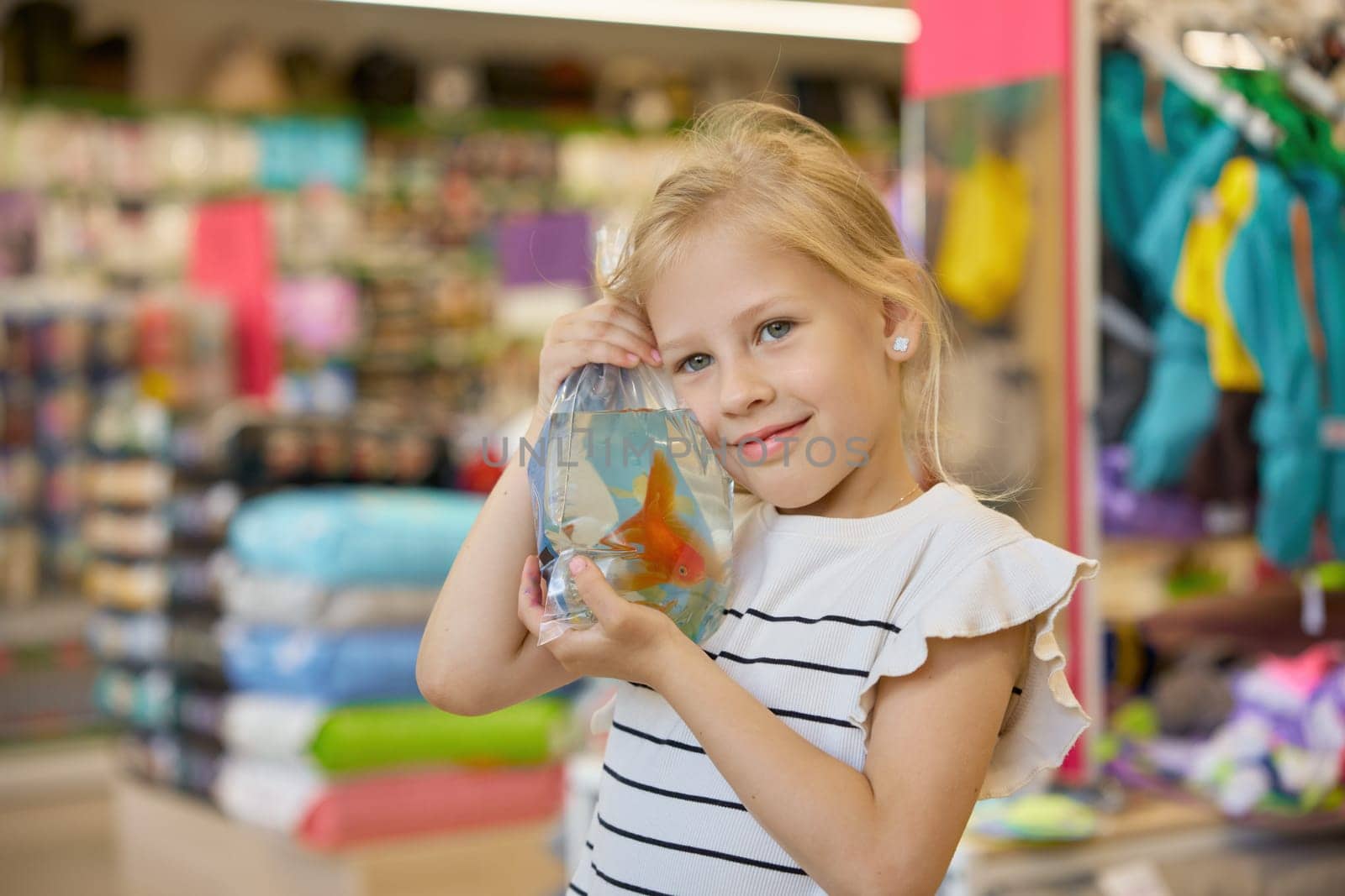 Portrait of cute smiling little girl holding packet with new gold fish pet standing over supermarket vet department store background