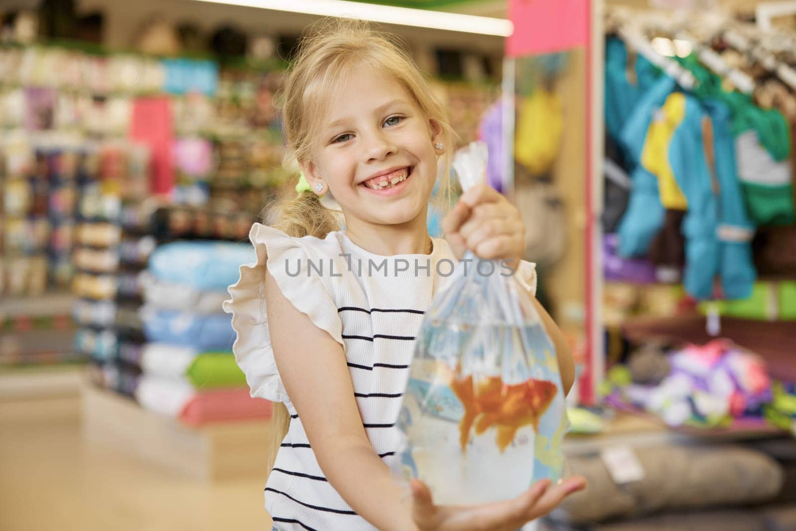 Portrait of cute smiling little girl holding packet with new gold fish pet standing over supermarket vet department store background