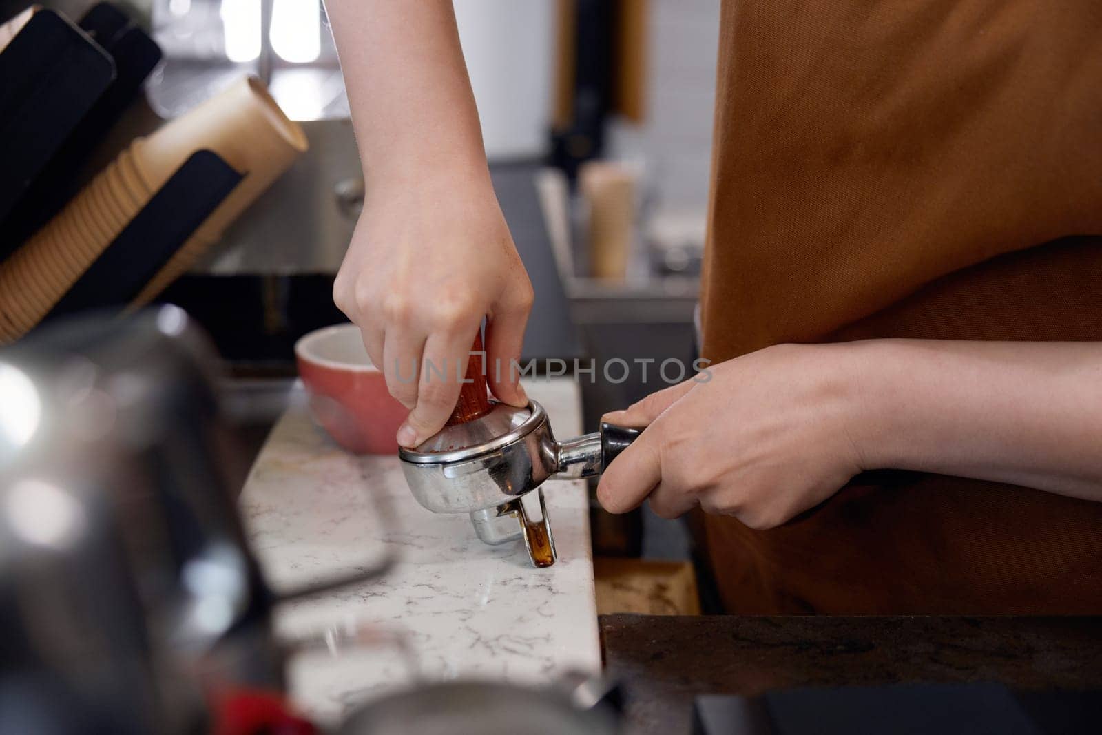Cropped shot of woman barista making coffee on counter in cafe. Closeup view on female hands holding coffee-maker machine equipment. Food and drink service concept
