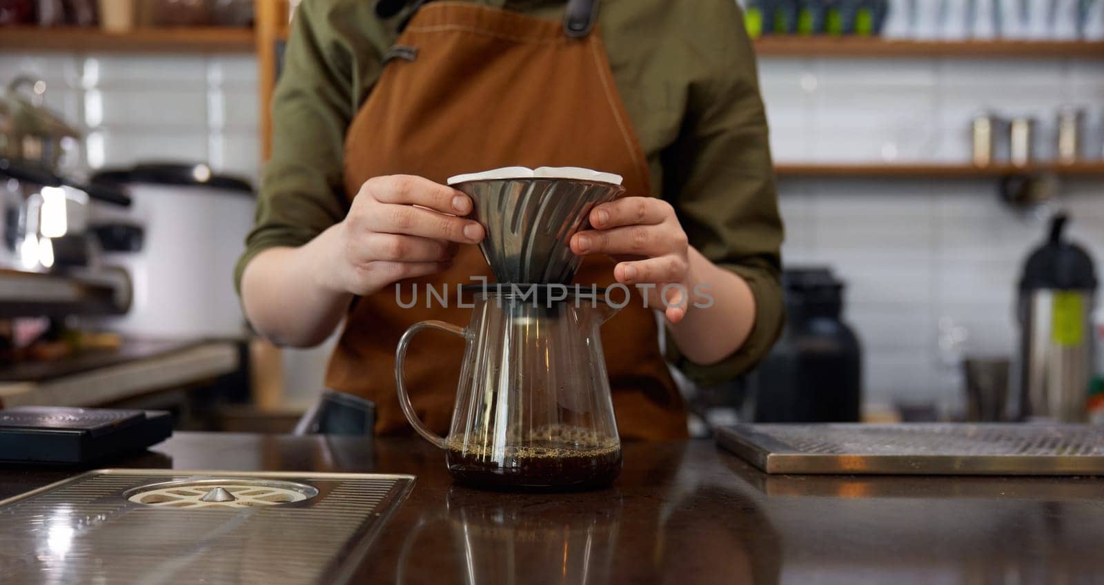 Experienced young woman barista using stainless steel funnel for coffee filtration. Manual extraction appliance for hot aroma drink preparation, Cropped shot