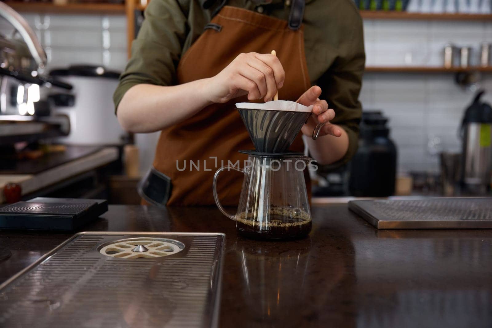 Experienced young woman barista using stainless steel funnel for coffee filtration. Manual extraction appliance for hot aroma drink preparation, Cropped shot
