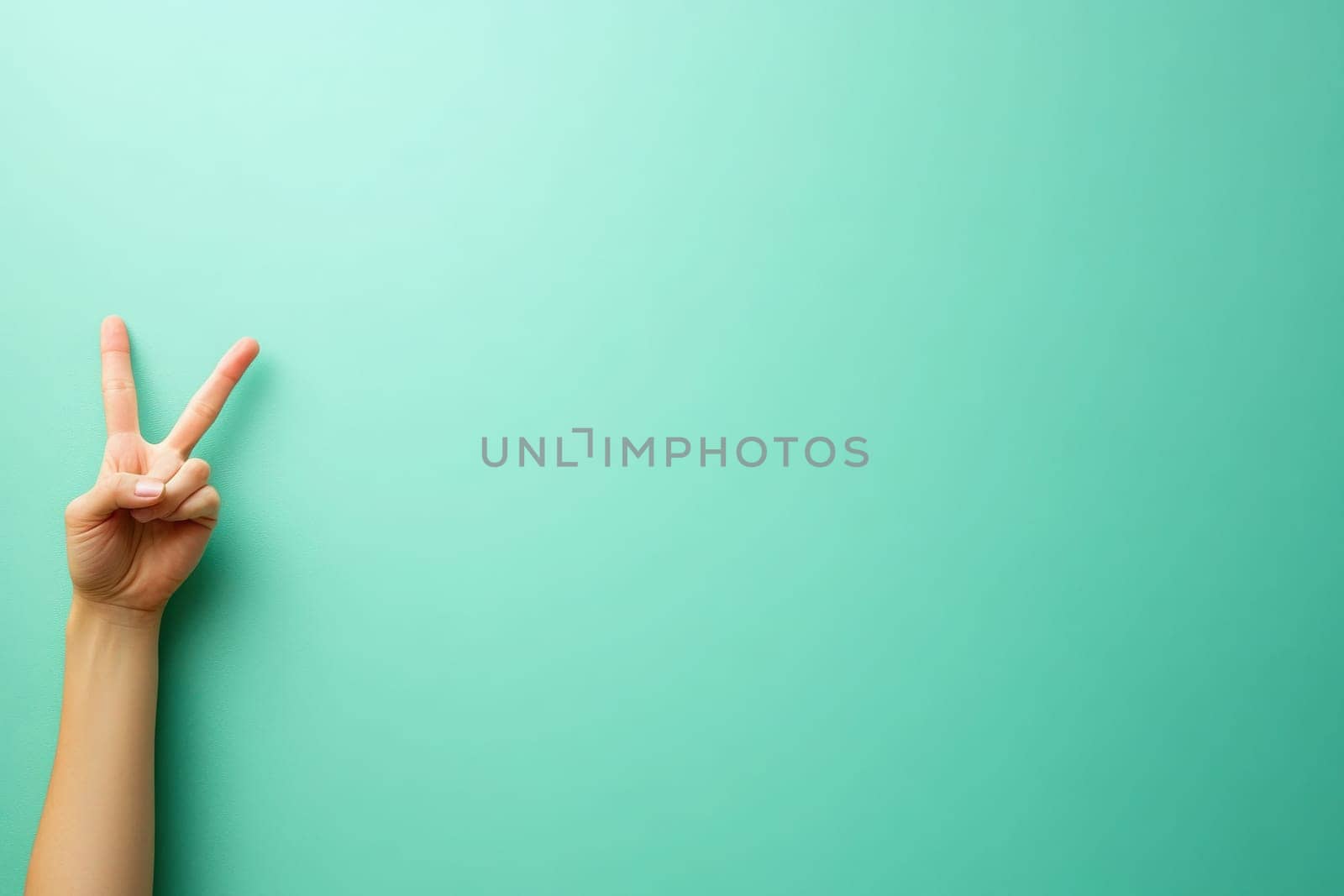 A hand is positioned to form a peace sign, standing out against a clean turquoise background. The simplicity of the gesture evokes feelings of tranquility and harmony.