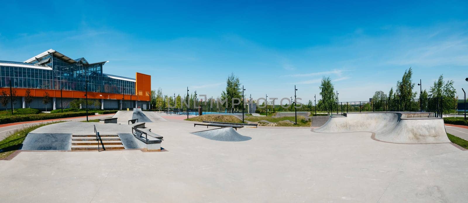 Panorama of empty public skateboard ramp park made of cement. Outdoors children's playground in skatepark for skateboarders, bmx riders and roller skates consisting of ramp, quarter, grindbox, rail