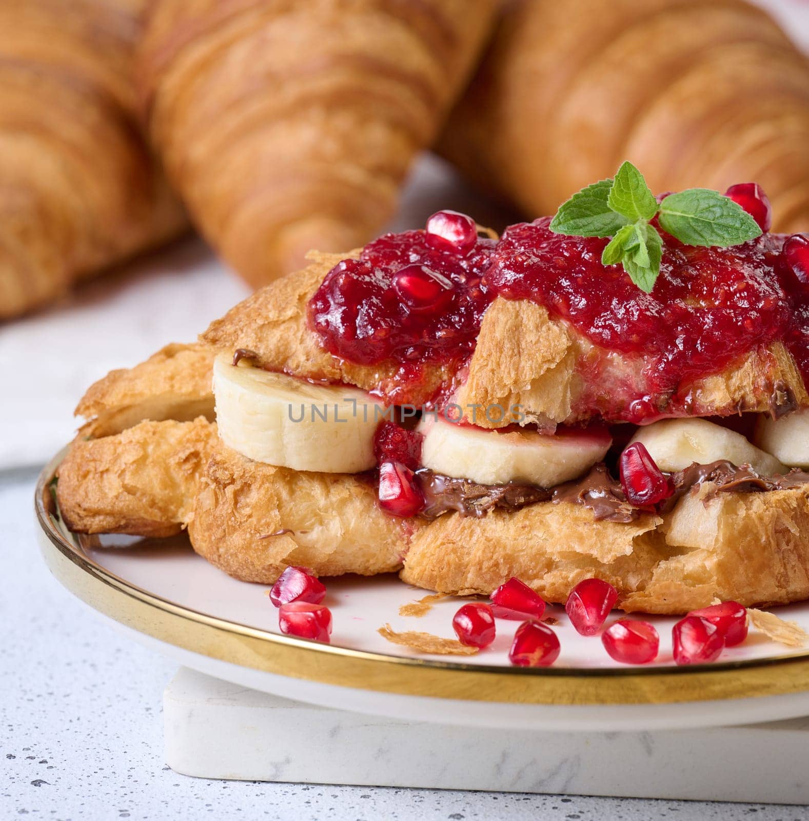 Croissant with chocolate, banana pieces and raspberry jam on a plate