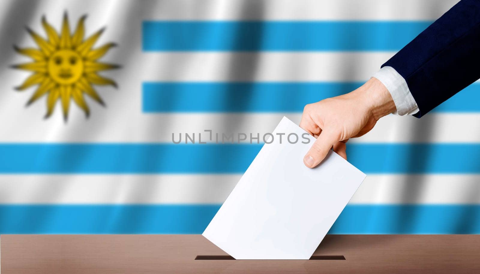 Uruguay Presidential elections. Hand holding ballot in voting ballot box with Uruguay flag in background