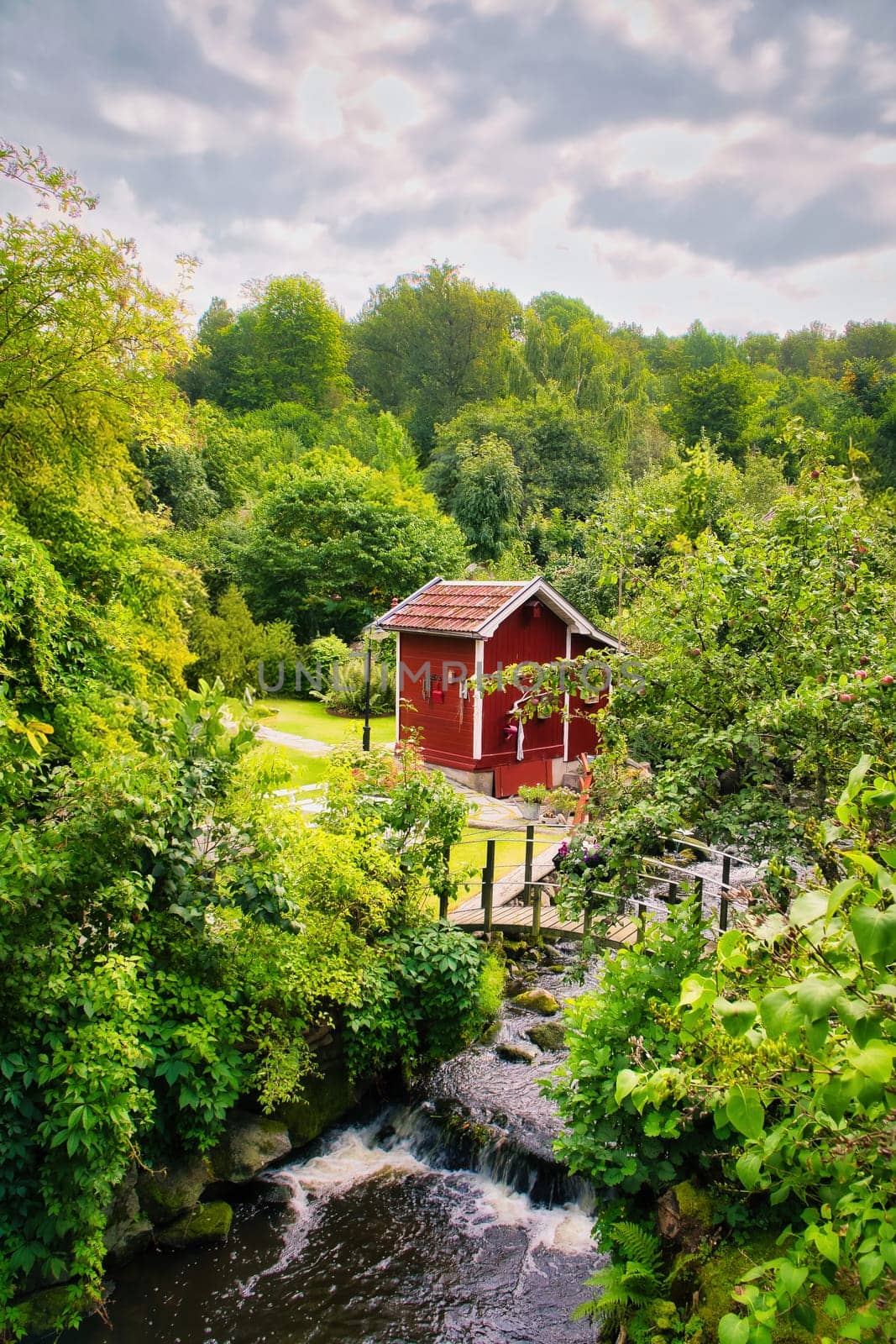 Stream with a small bridge in front of a red wooden house in Sweden. Trees on the bank . Scandinavian nature