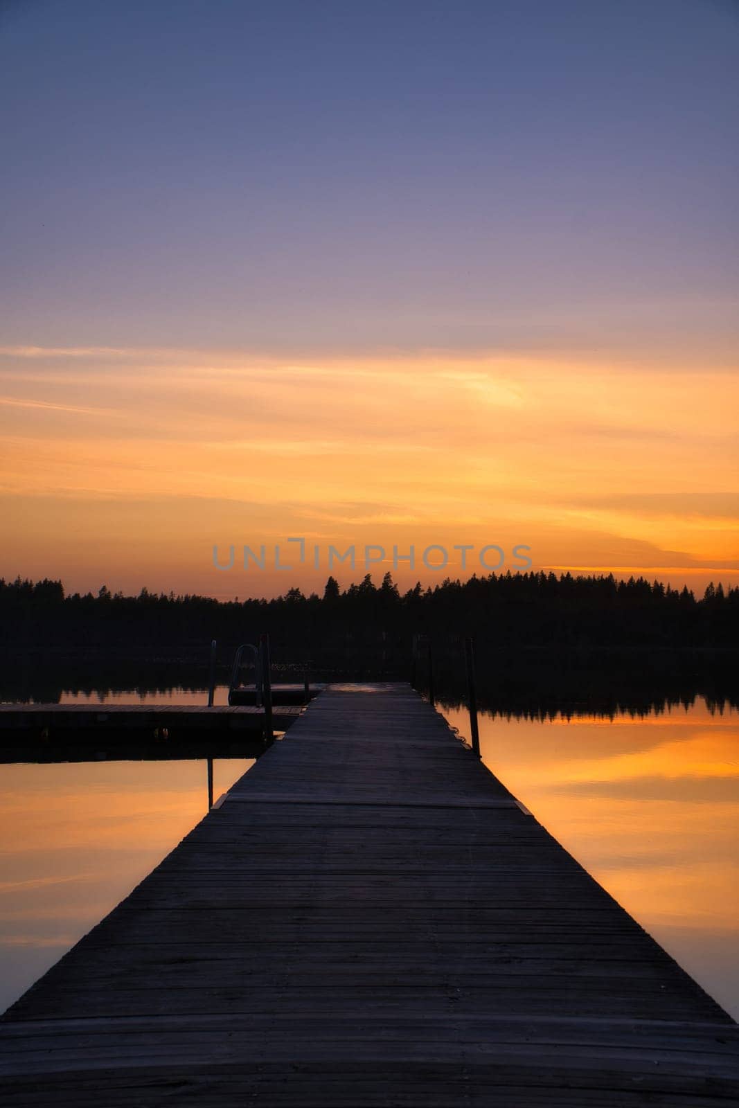 Wooden jetty at sunset on a Swedish lake. The colors of the sunset are reflected in the water. A bathing lake in the Scandinavian countryside
