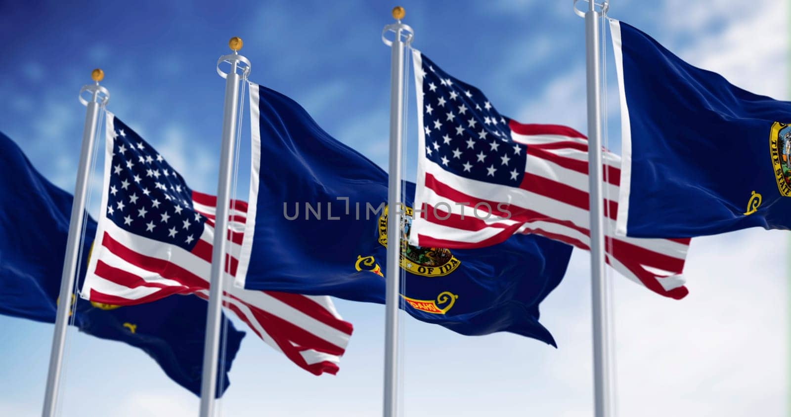 The Idaho state flags waving along with the national flags of the United States of America on a clear day. 3D illustration render. Rippled fabric. Selective focus
