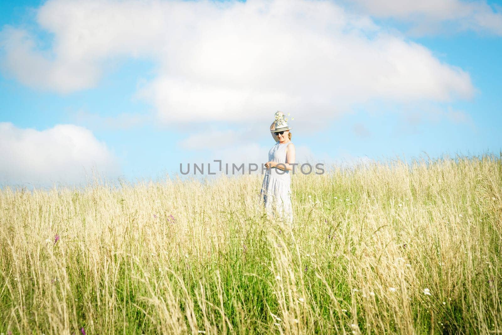 Happy mature woman with wildflowers in a tall grass field on a bright summer day.
