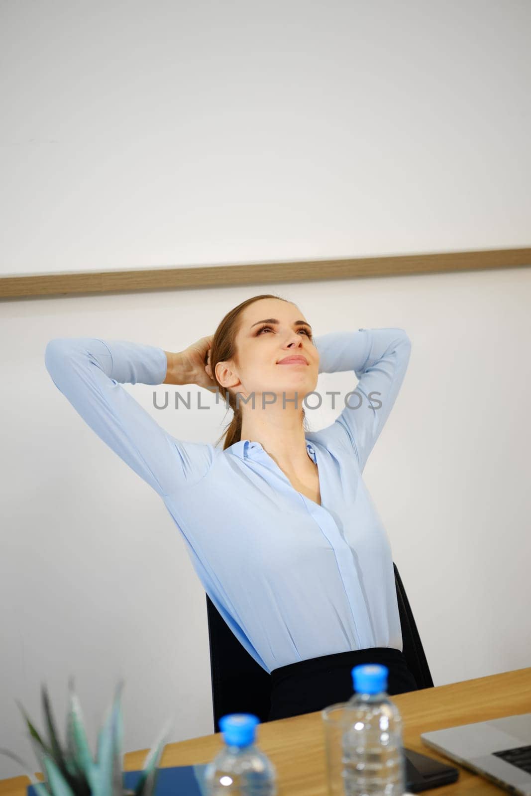 A woman sits comfortably at her desk in a contemporary office, stretching and enjoying a moment of relaxation. She appears to be taking a break, reflecting a peaceful atmosphere in the workspace.