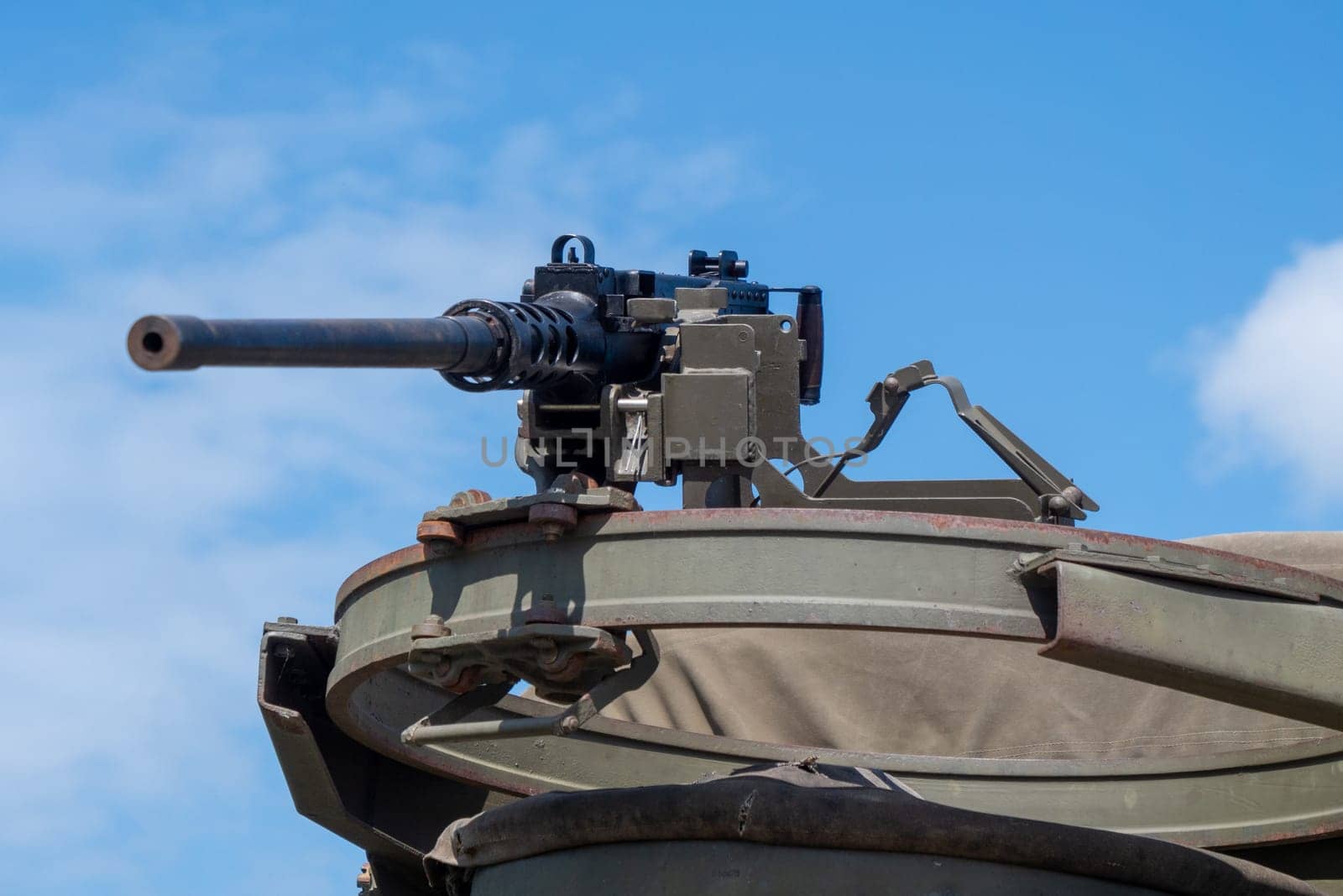A machine gun is on a metal object with a green cover. The gun is pointed at the camera