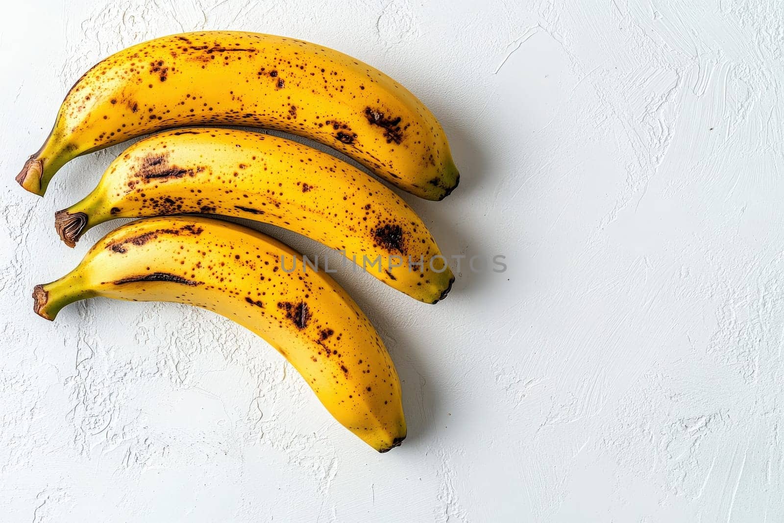 Three ripe bananas with slight brown spots are neatly placed on a solid white background, highlighting their vibrant yellow color and texture, perfect for a healthy snack or recipe.