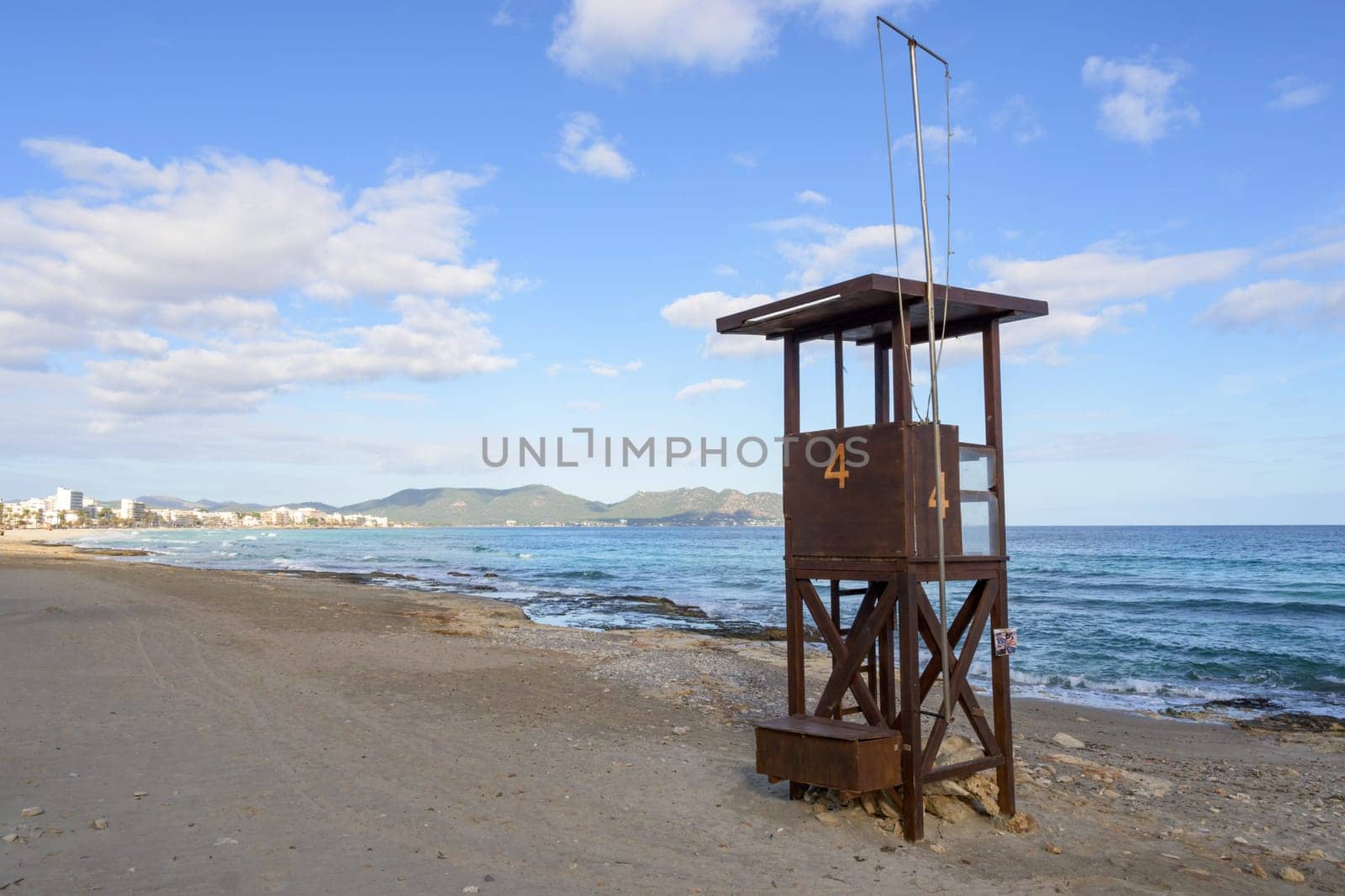 A rustic lifeguard tower stands on a beach overlooking the ocean and distant mountains, mallorca balearic islands, spain