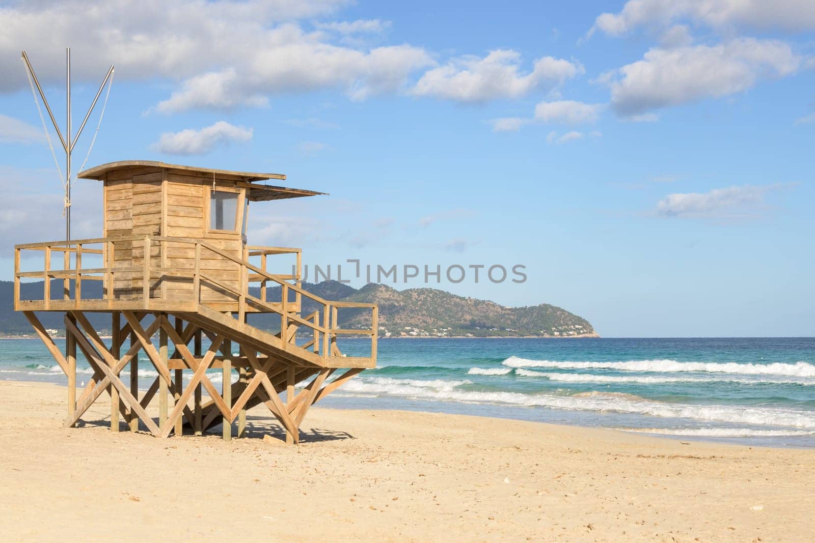 A wooden lifeguard tower on a sandy beach with ocean waves and mountains in view, mallorca balearic islands, spain
