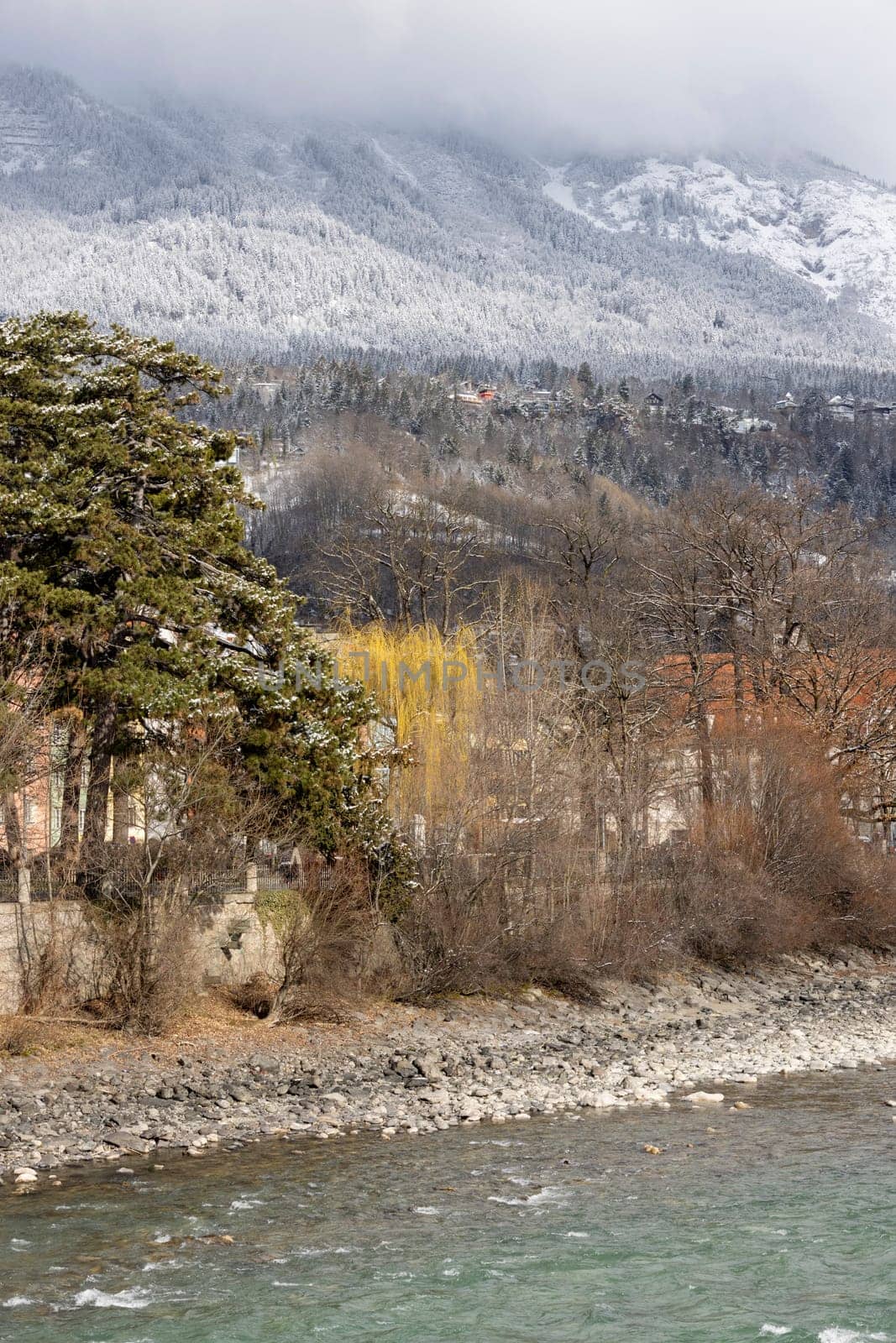 River Inn, snow covered slope of Alps in the clouds in dinstance, Innsbruck, Austria