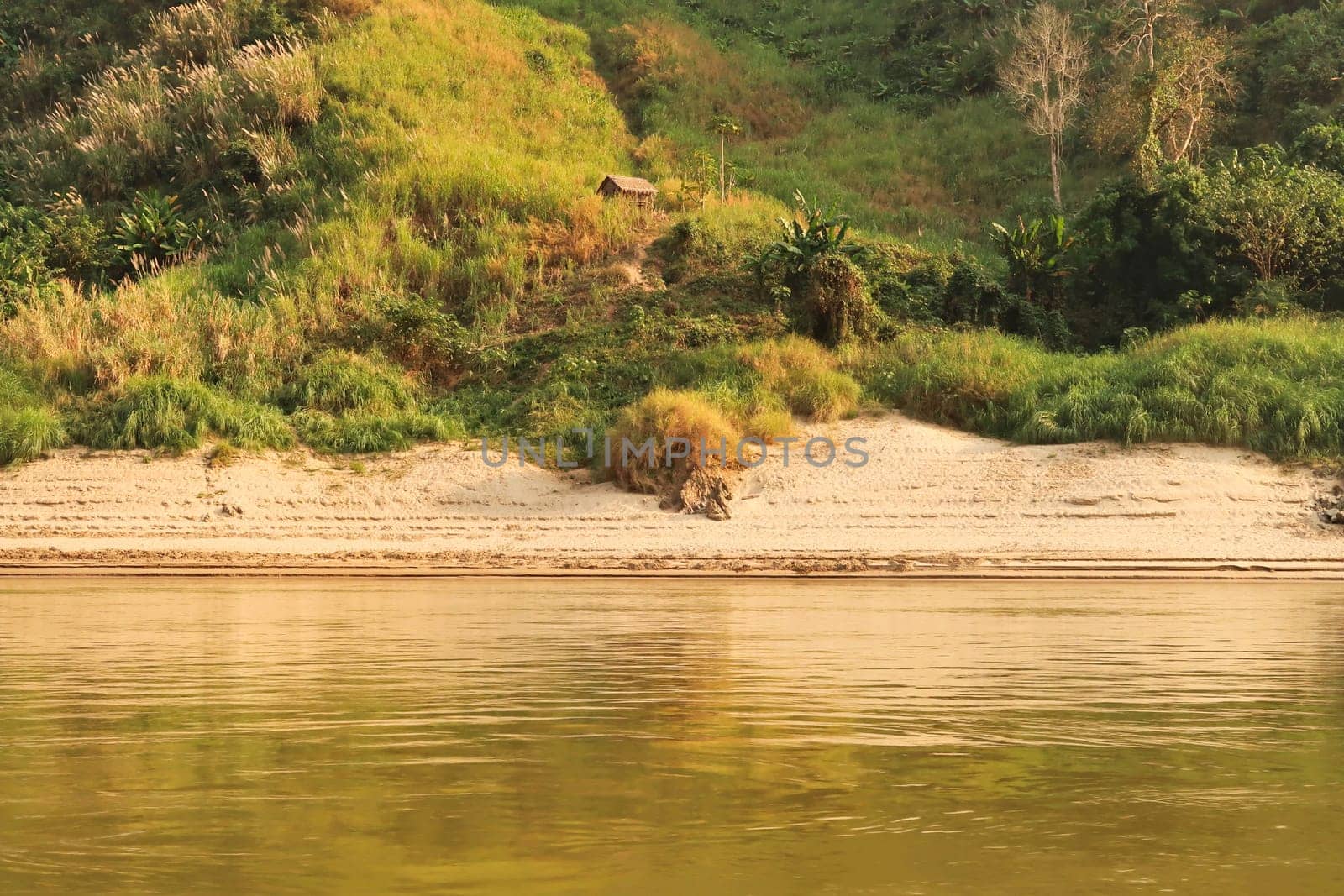 View from the slow boat from Thailand to Laos onto the shore of the Mekong River, a trail is leading up to a small hut, cabin, Laos 2023