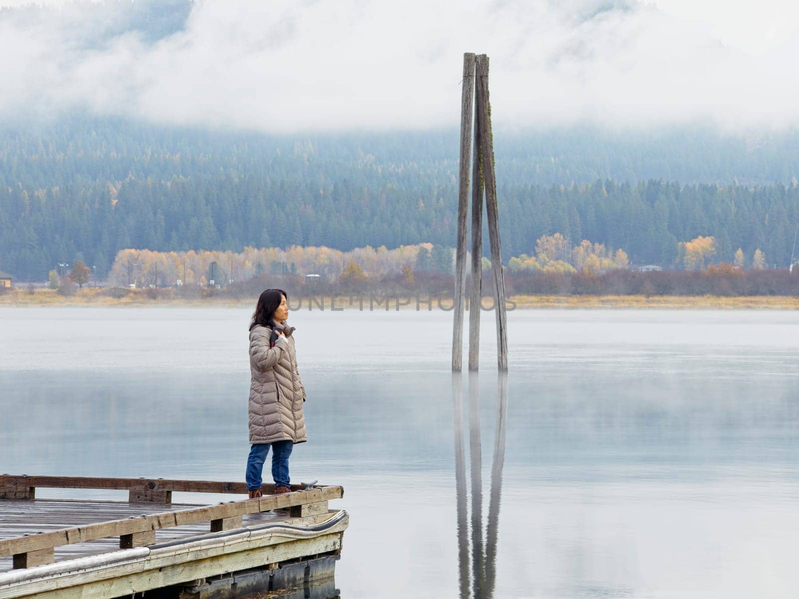 A woman stands at the edge of a dock gazing out at the calm Pend Oreille River on a cold morning in eastern Washington.