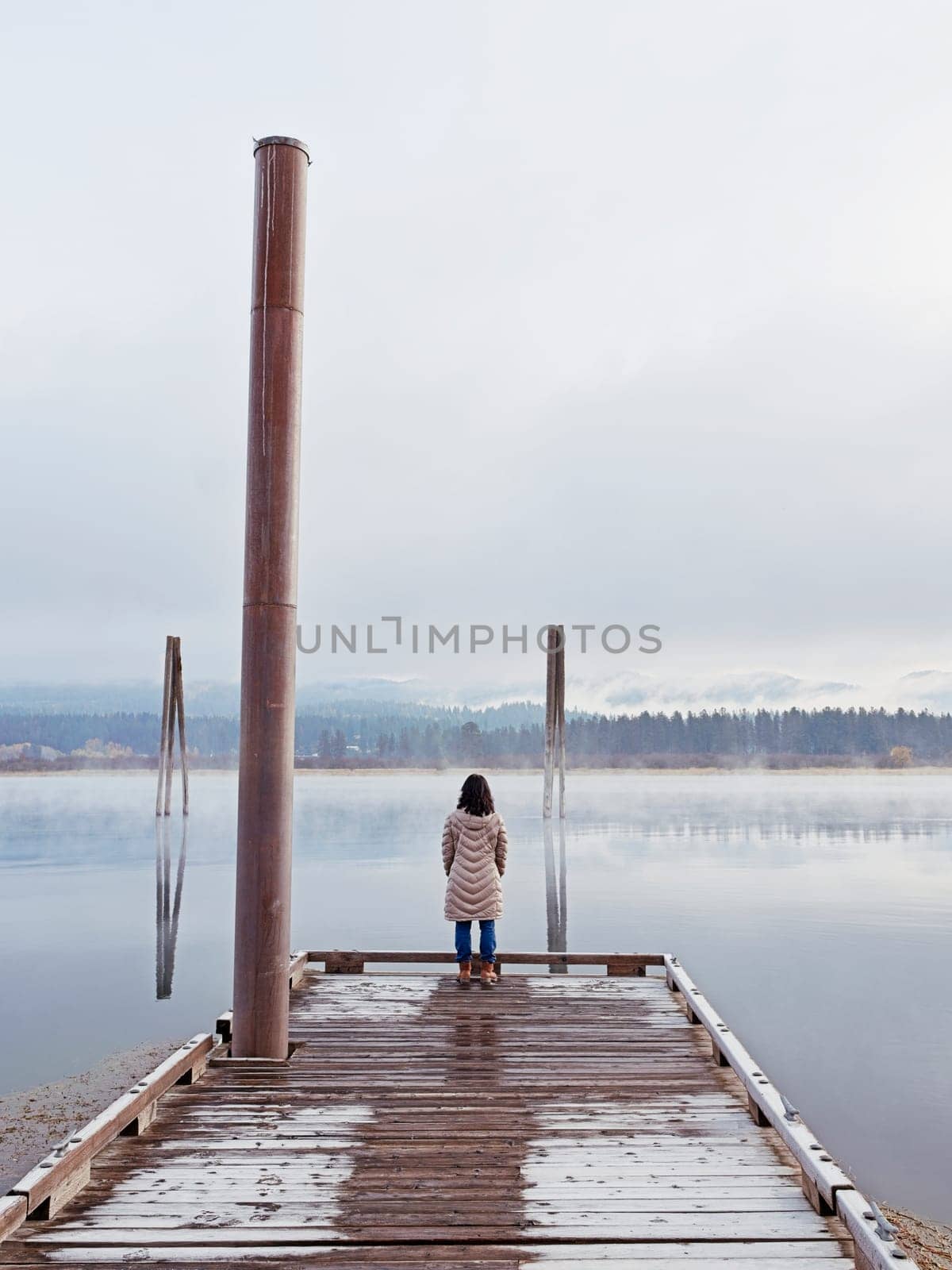 A woman in a coat stands at the end of a dock looking out at the Pend Oreille River in eastern Washington.