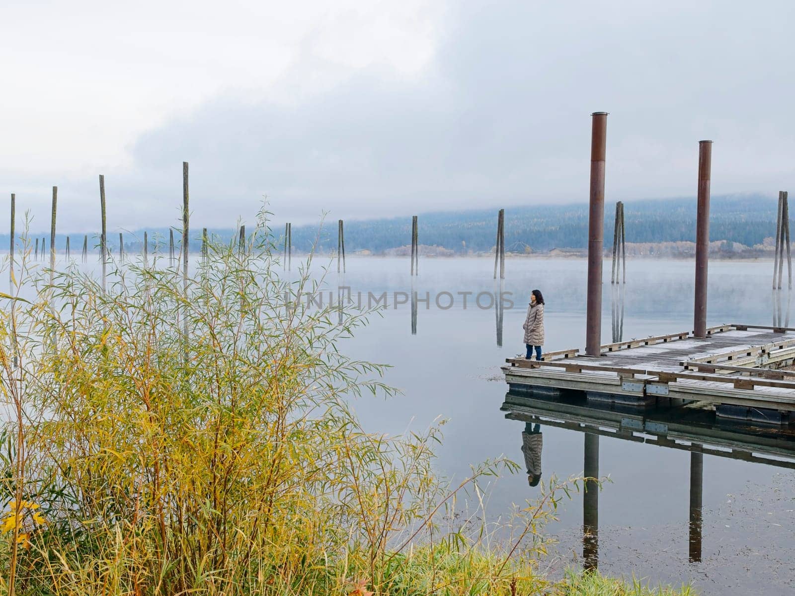 A landscape photo of a woman standing on a dock looking out at the calm water of the Pend Oreille River in eastern Washington.