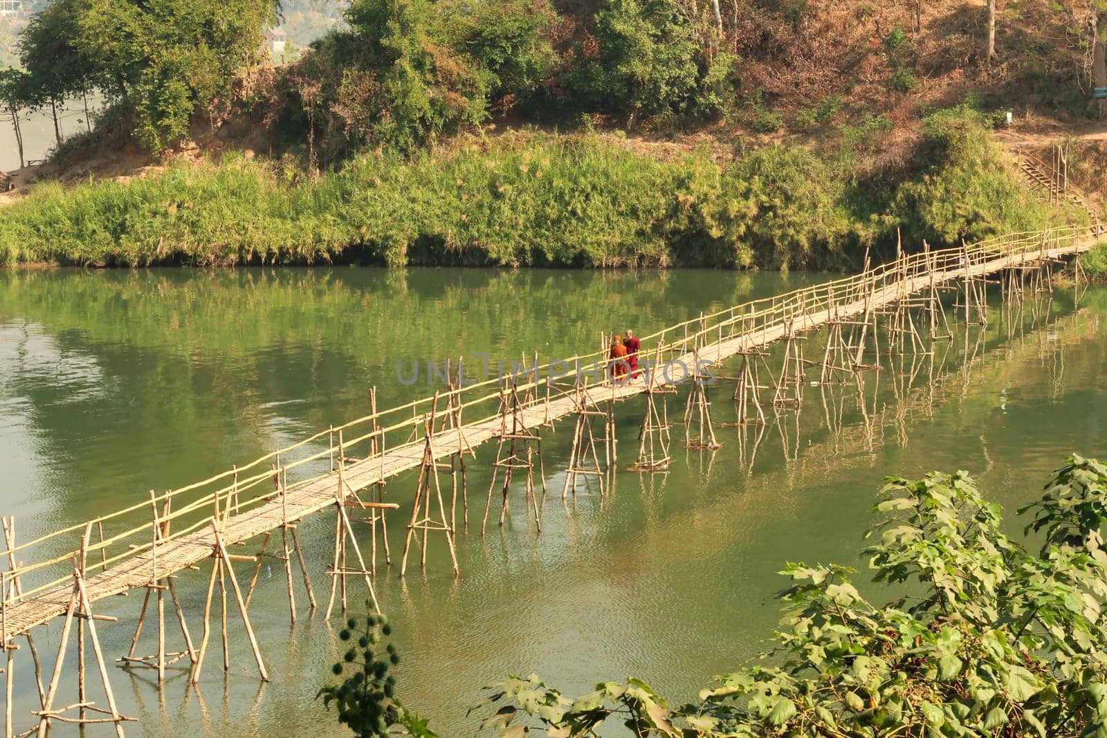 Two buddhist monks cross a traditional bamboo bridge over the Nam Khan River in Luang Prabang, Laos 2023