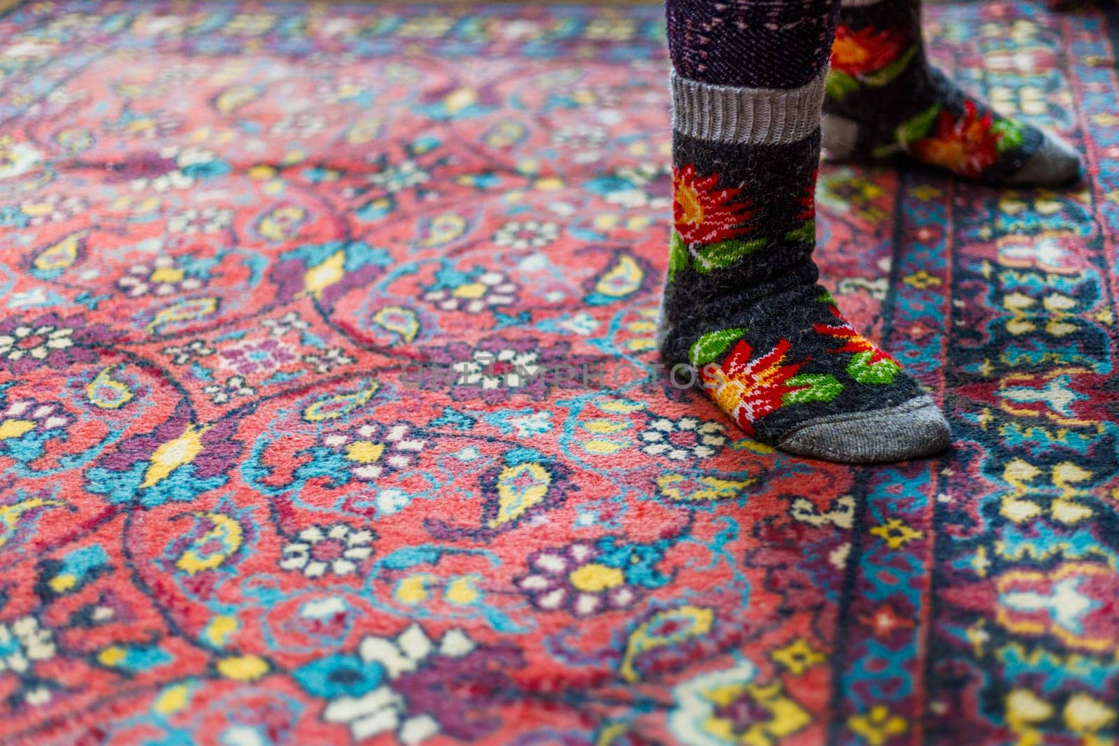 legs in warm woven wool socks standing on red ornate carpet floor at home backlit with a window light