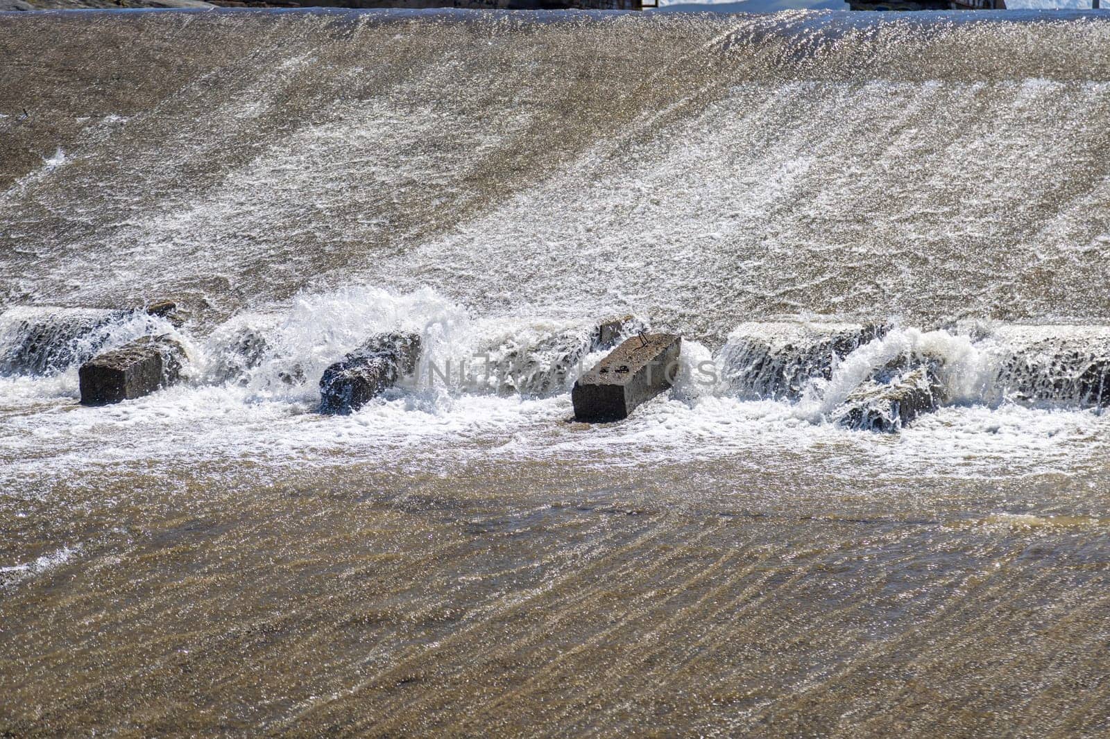 row of chute dentate blocks in concrete water spillway channel slope slowing down the flow of water running down.