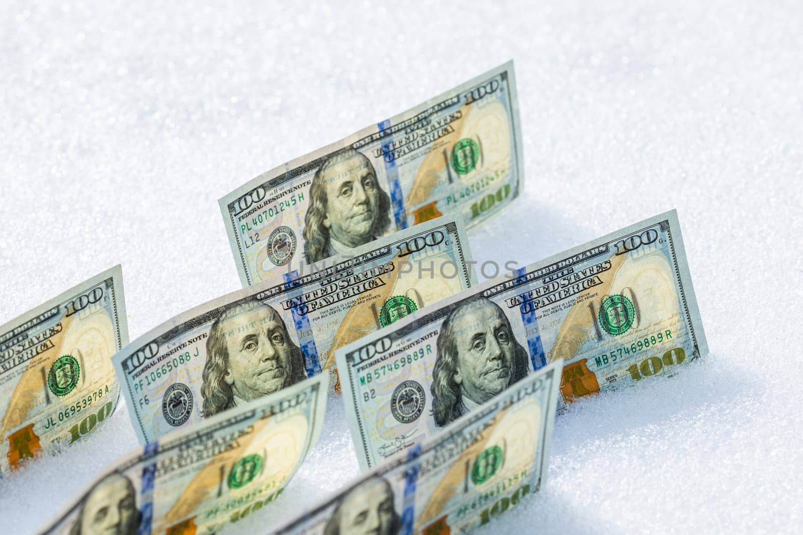 hundred us dollar banknotes standing on their side on the snow surface at sunny winter day