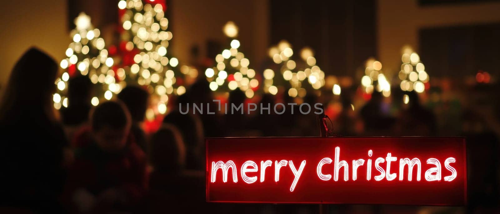 Soft lights illuminate beautifully decorated Christmas trees while a cheerful sign wishes everyone a Merry Christmas during a holiday gathering.
