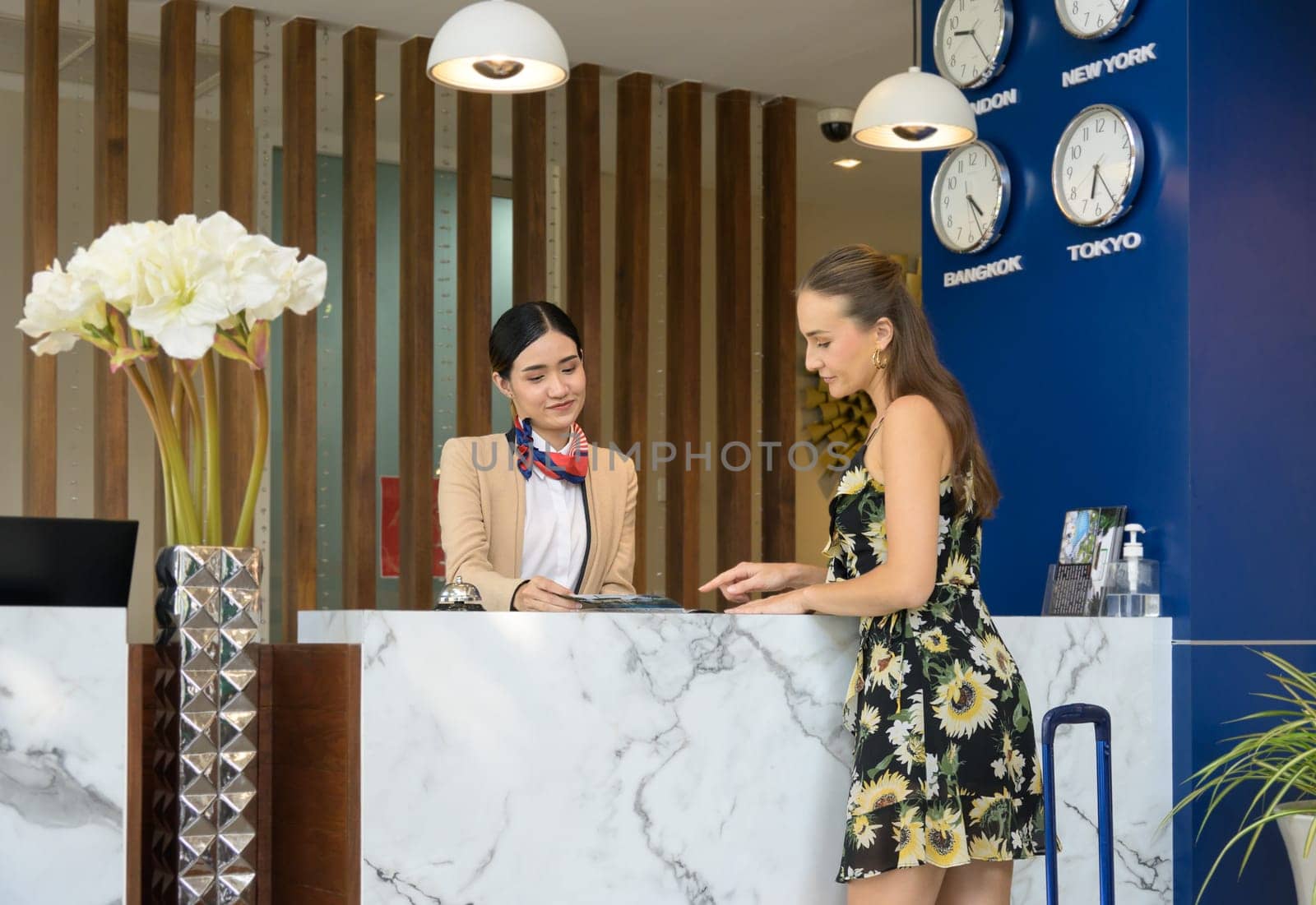Friendly young receptionist helping and giving hotel check in information service to attractive female guest upon arrival