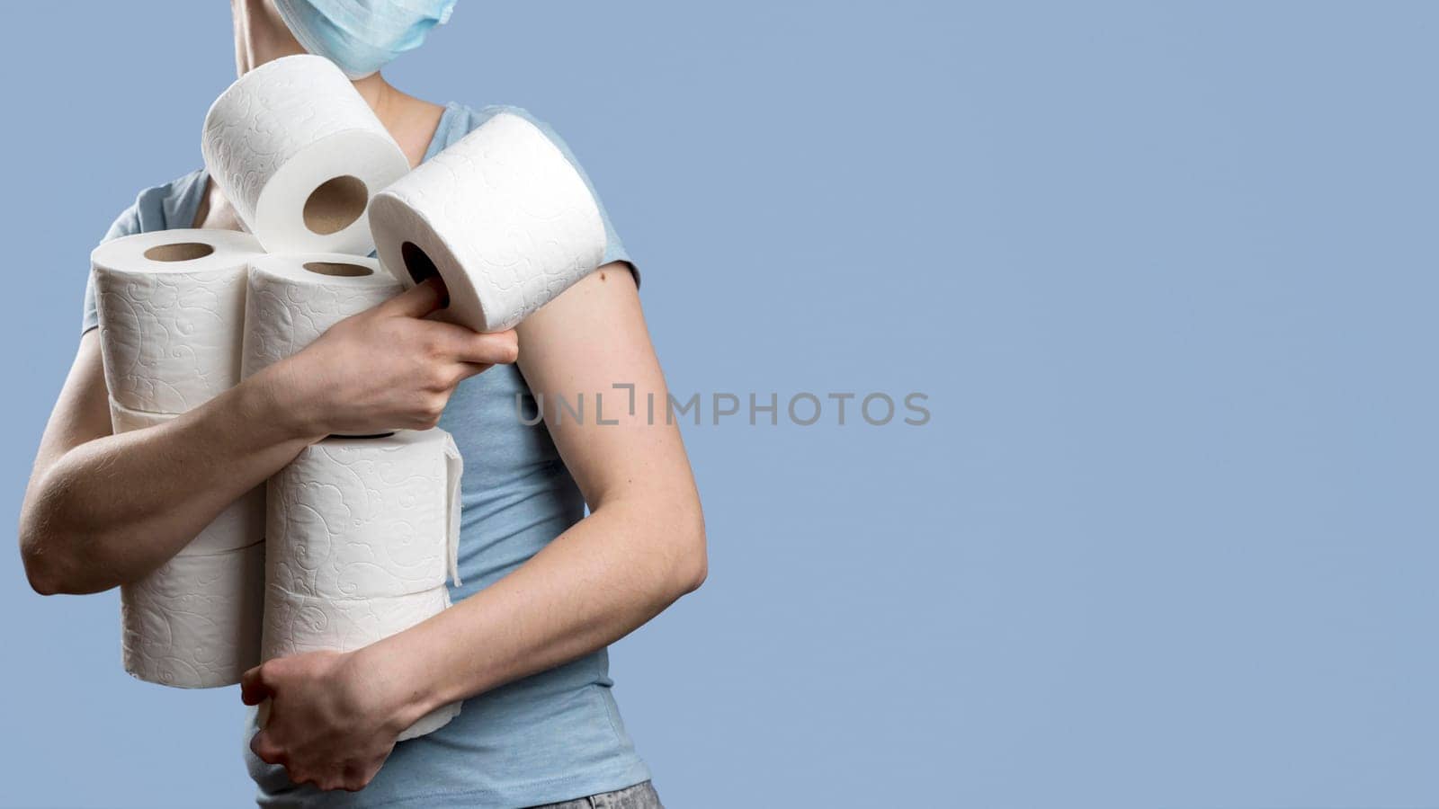 side view woman holding many toilet paper rolls while wearing medical mask. High resolution photo