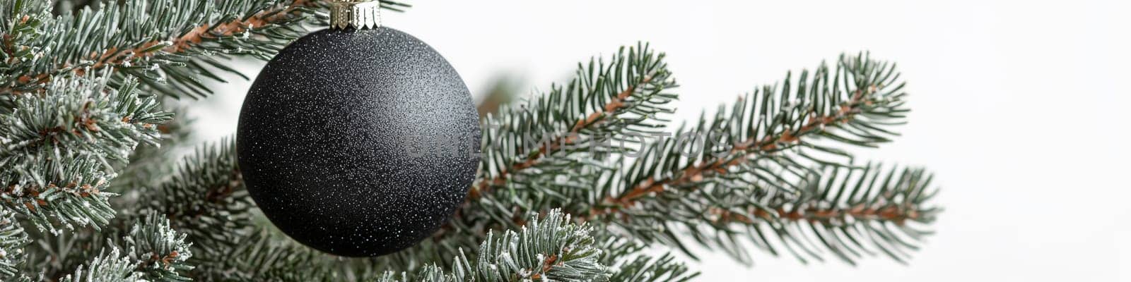 A refined close-up image of a glossy black Christmas ornament hanging on a lush green pine branch, set against a crisp white background. The minimal design offers a stylish, modern look, leaving space for text or branding, ideal for holiday promotions or seasonal messaging.