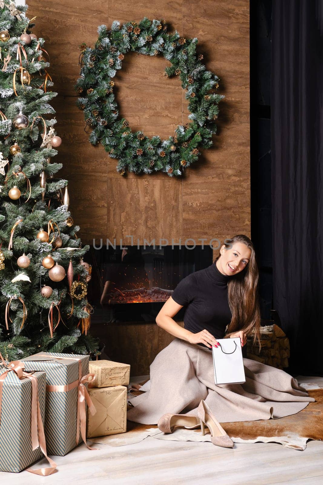 Lovely woman looks inside the gift package sitting on the floor by the fireplace