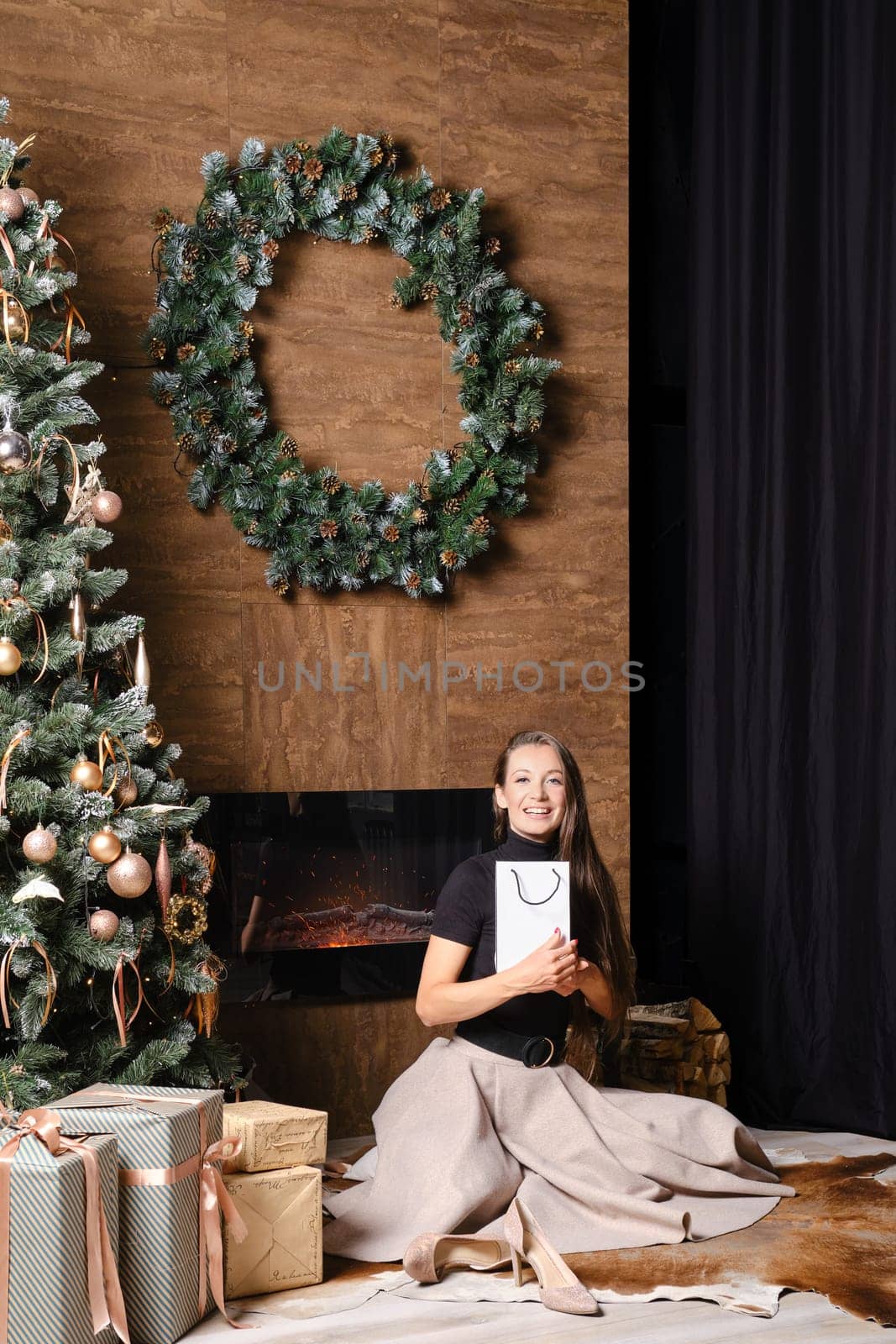 Happy woman sitting on the floor by the fireplace hugging a gift in her hands