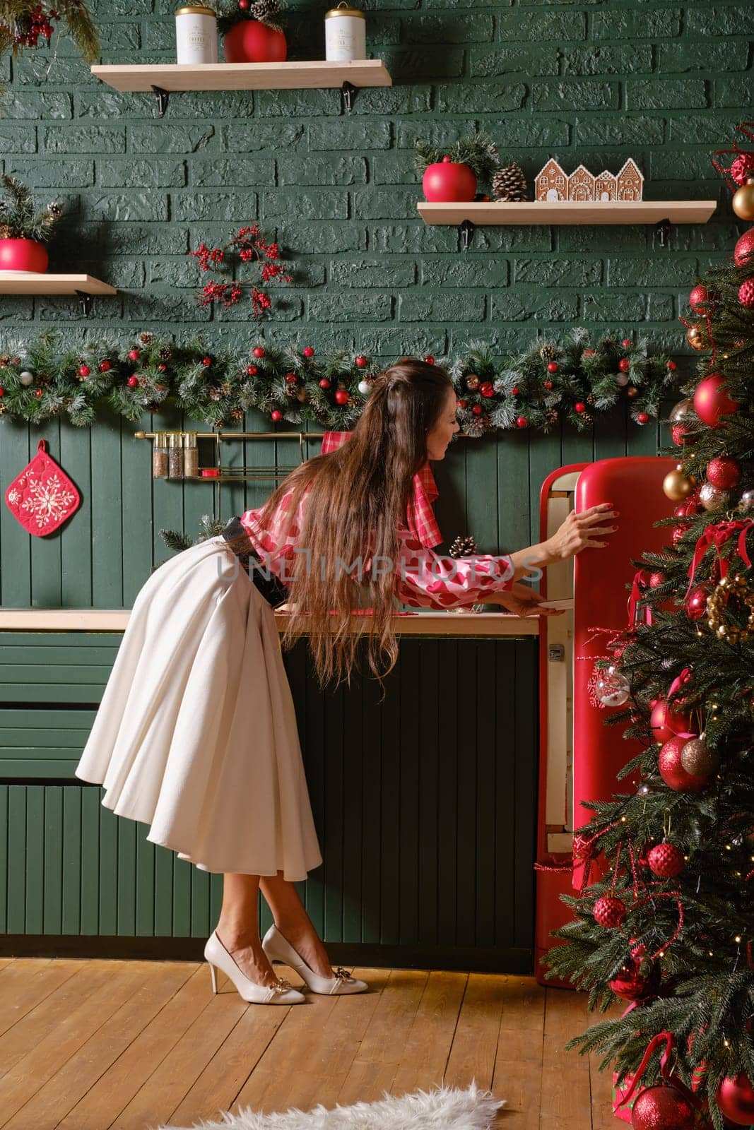 A woman opening a vintage red refrigerator amidst a beautifully decorated Christmas-themed kitchen. The kitchen is decorated with holiday ornaments, giving the space a warm and inviting atmosphere