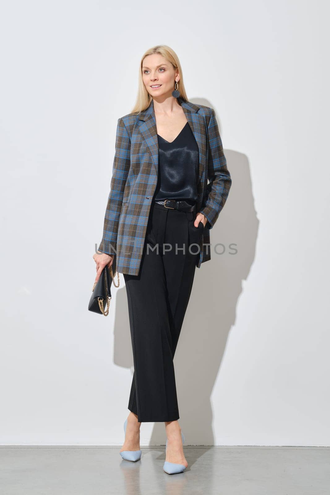 Modern businesswoman in stylish checkered jacket and loose trousers holding handbag