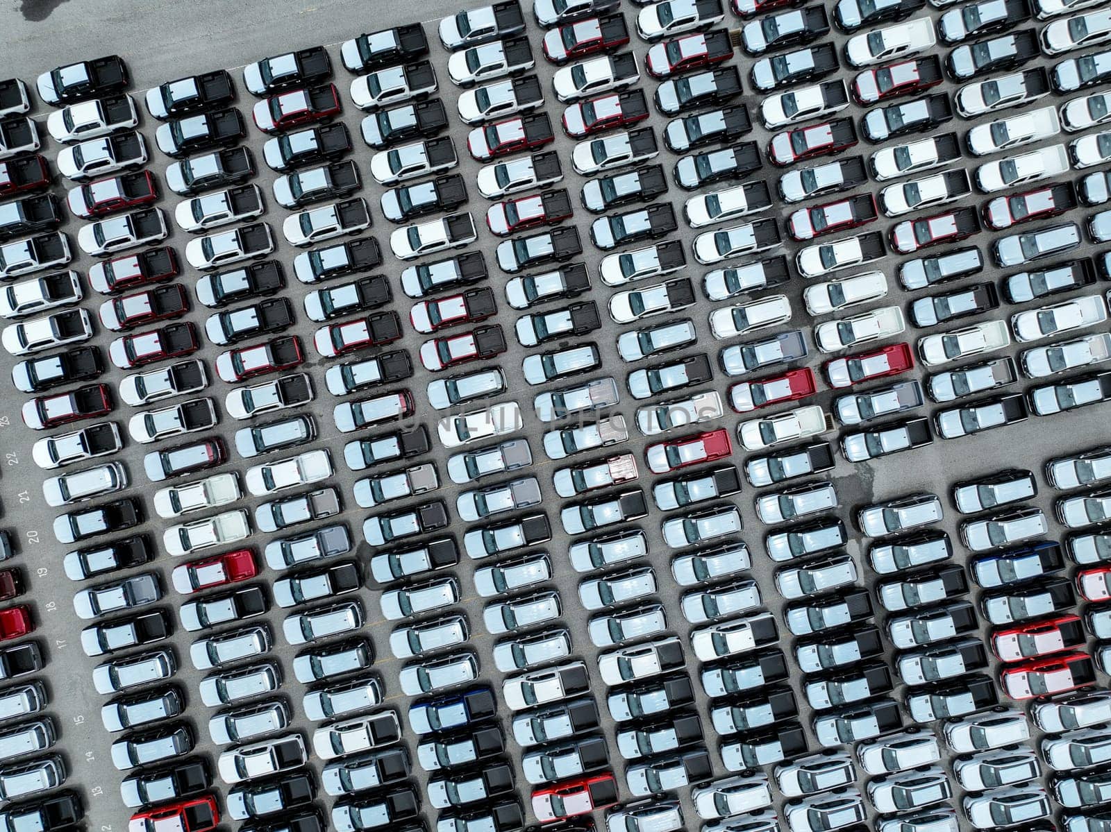 Aerial view of new cars stock at a large factory parking lot. Automotive industry, logistics operations, and vehicle storage for import and export. Key role in the global car market supply chain.