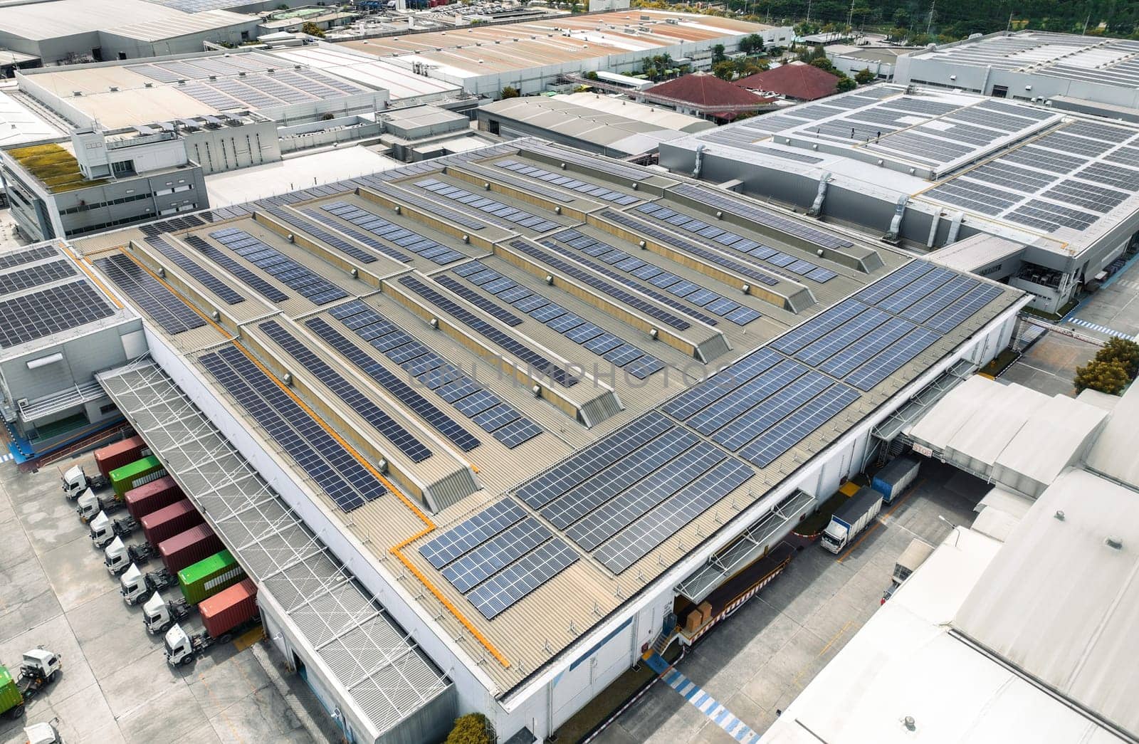 Solar-powered warehouse facility with freight trucks at loading docks. Eco-friendly logistics and efficient cargo transportation. Solar panels and sustainable energy concept in distribution center.
