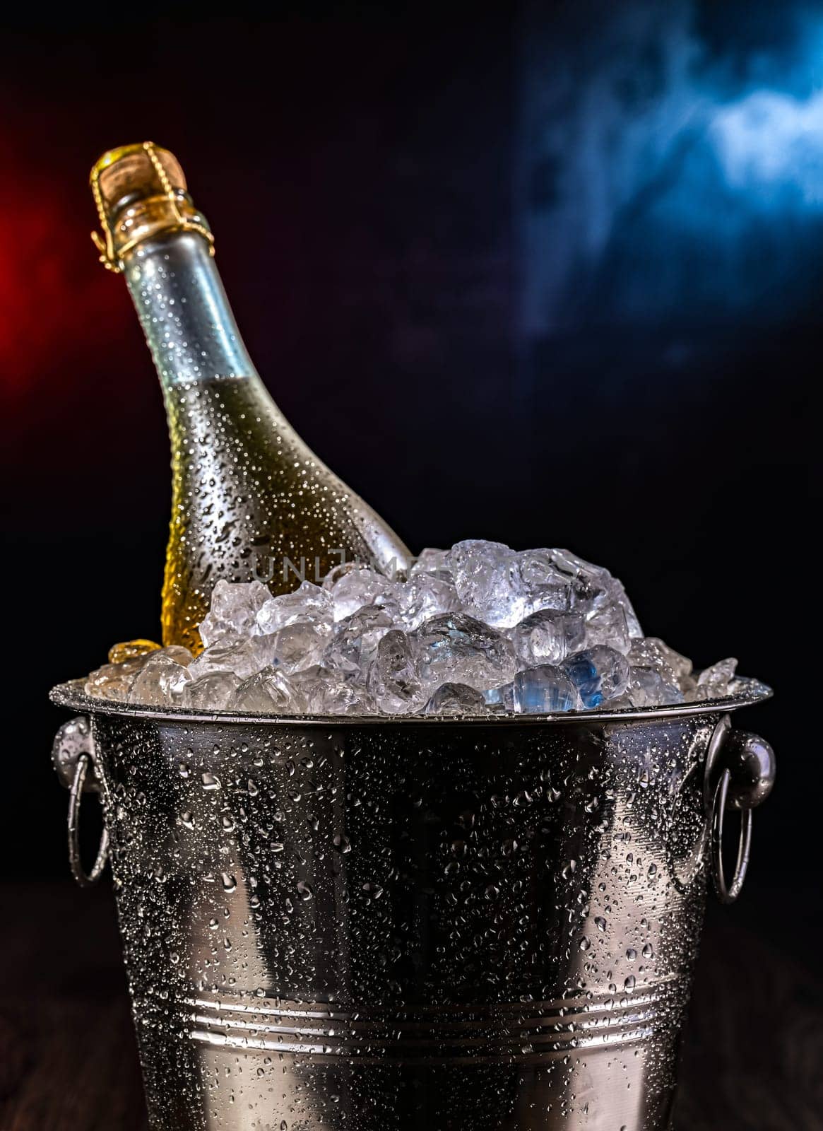 Bottle of sparkiling wine in bucket with crushed ice.