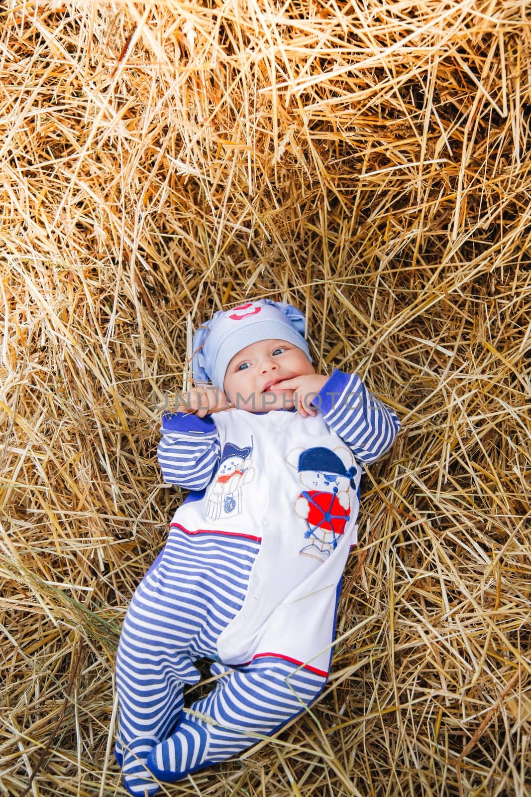 A cute little baby peacefully lying in a bed of straw, wearing a charming outfit along with a lovely hat