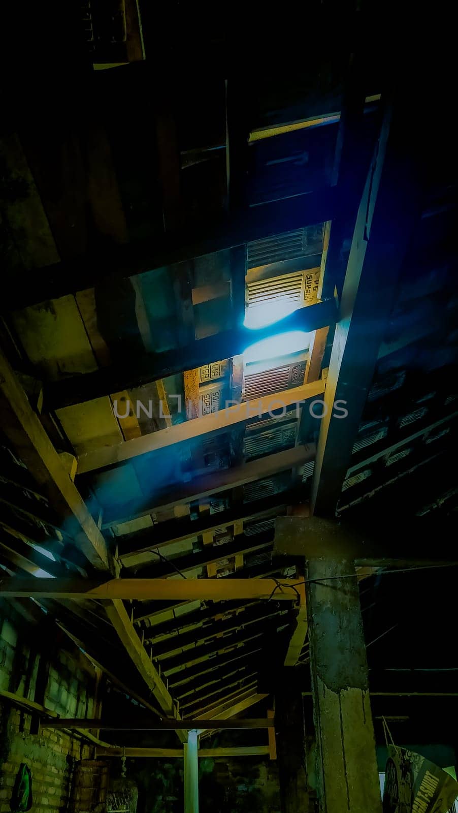 Atmospheric light beams penetrate an old wooden roof, creating a mysterious and rustic ambiance. The aged structure and shadows add a sense of history and intrigue to the scene.