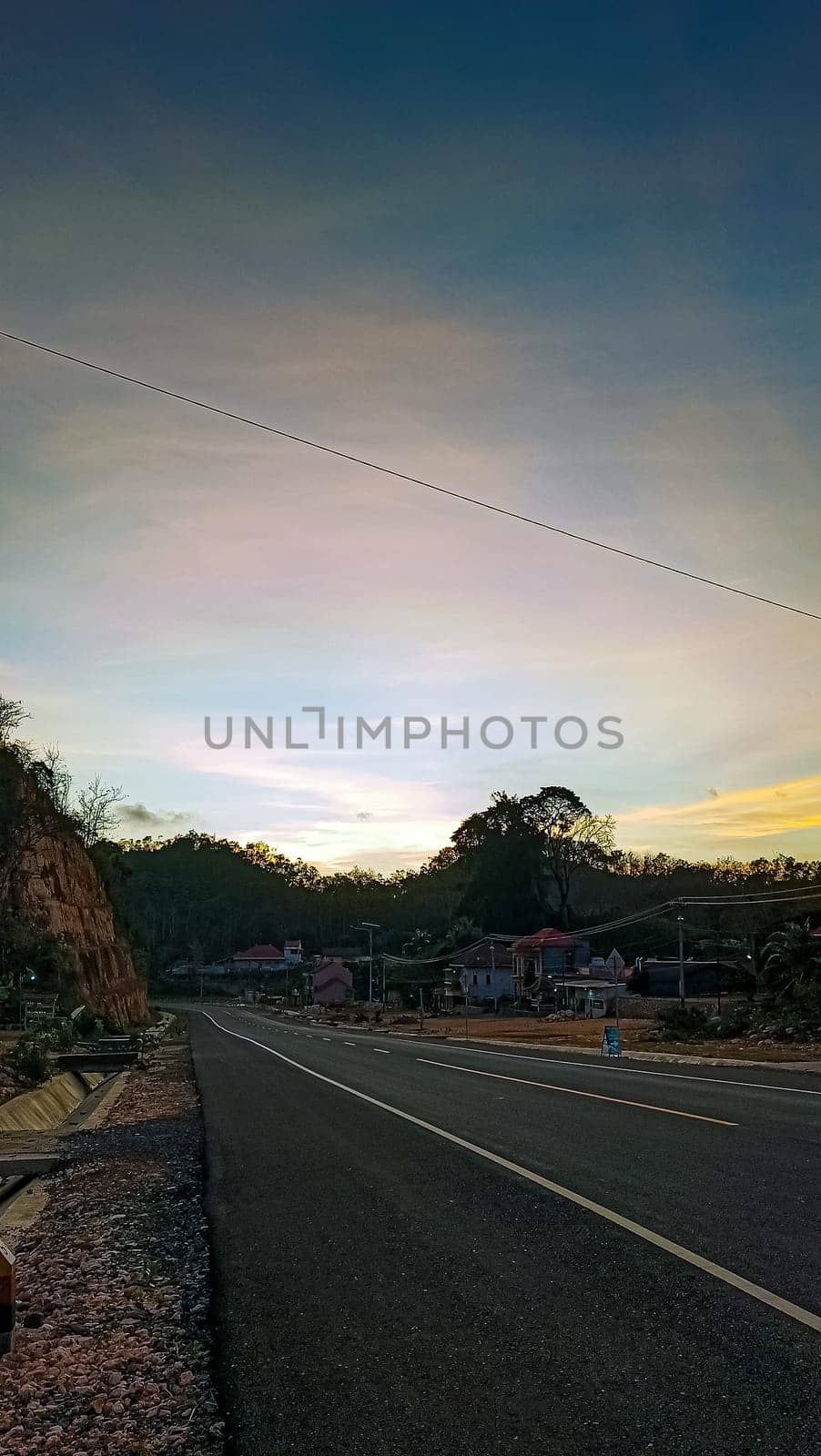 A serene landscape showcasing a quiet rural road with a stunning sunset in the background. The peaceful countryside setting evokes tranquility and the beauty of nature.