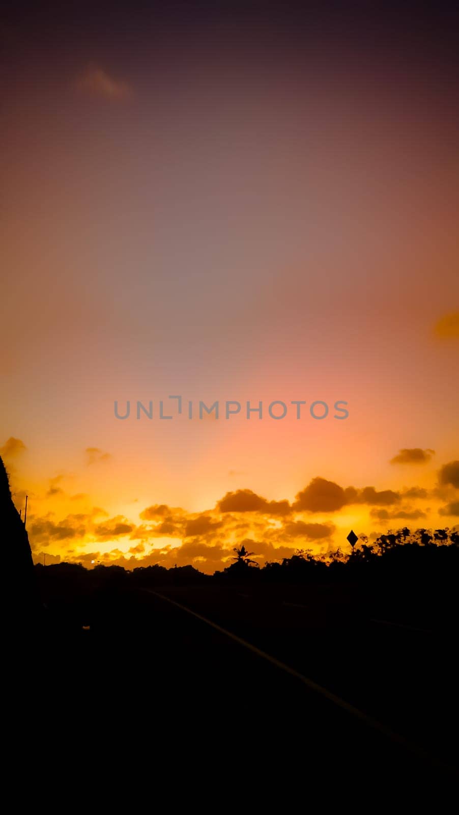 A breathtaking view of a golden sunset casting warm hues over a tranquil countryside road, creating a peaceful and calming atmosphere.