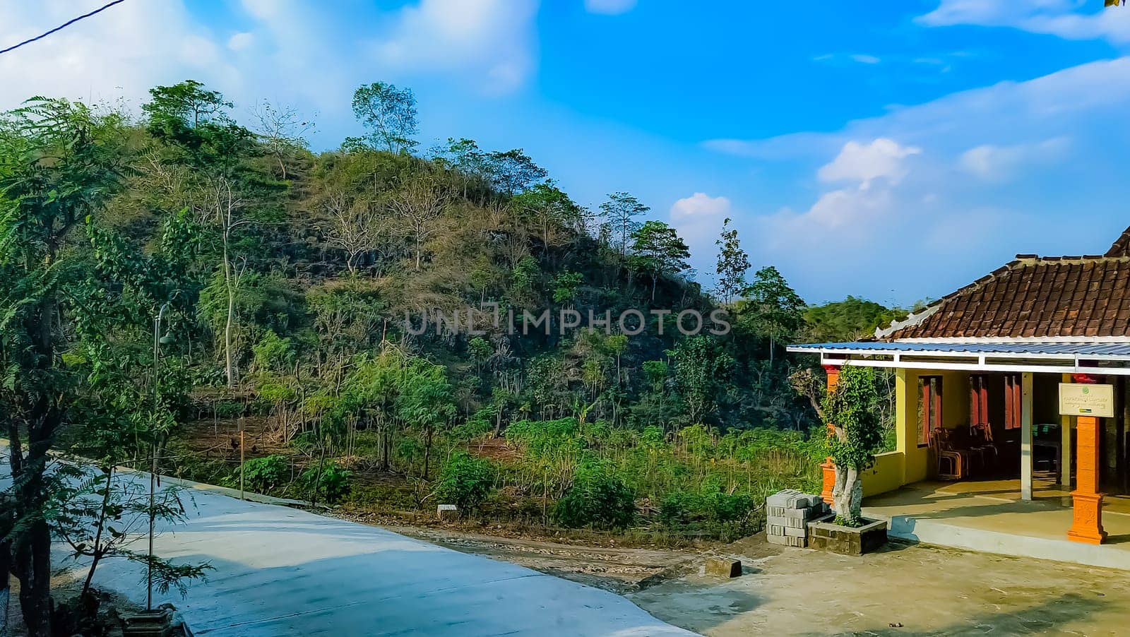 A serene countryside house surrounded by lush vegetation and rolling hills under a bright blue sky, evoking tranquility and natural beauty.