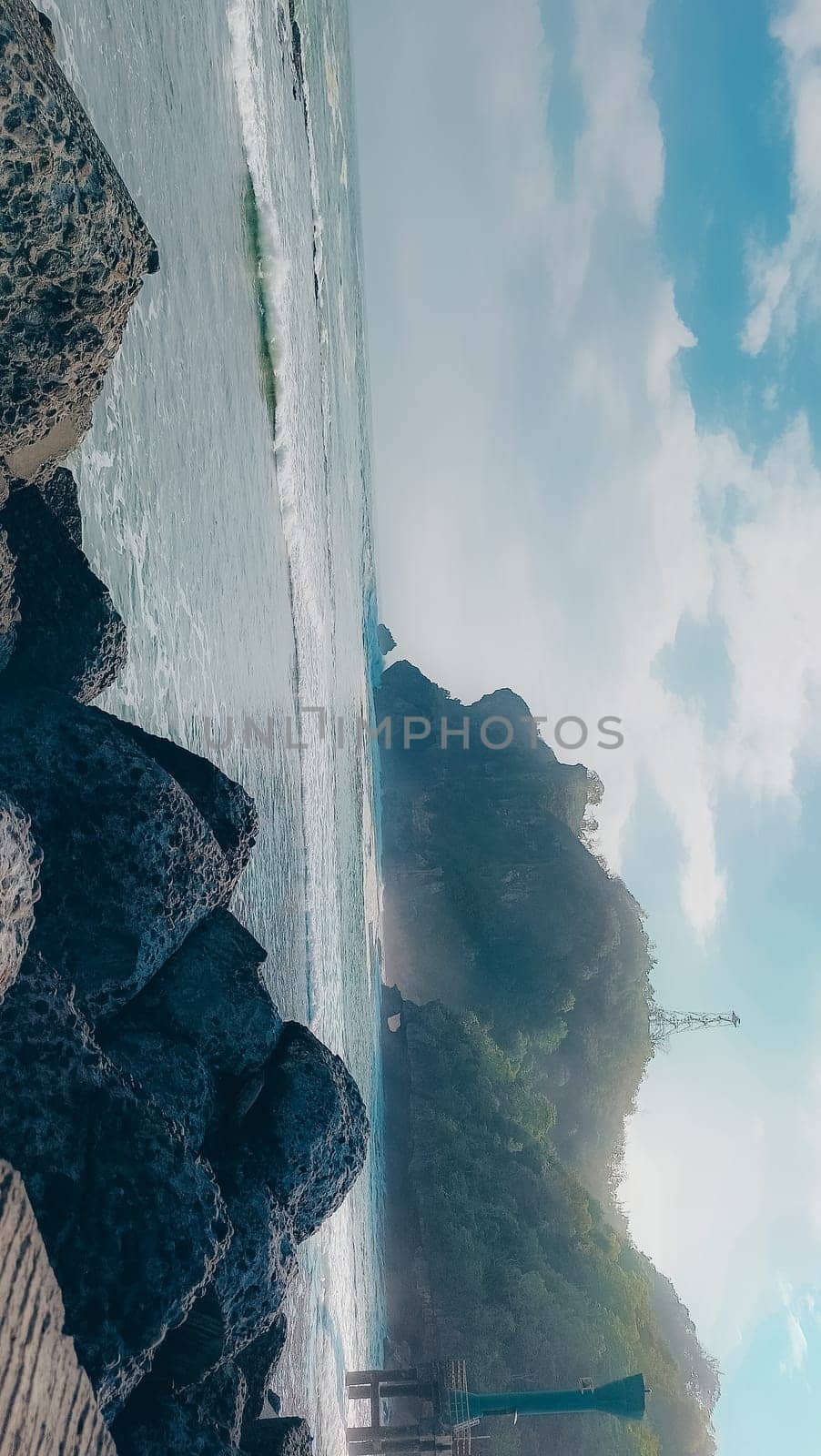 A rocky shoreline with a large rock formation in the background. The water is calm and the sky is blue