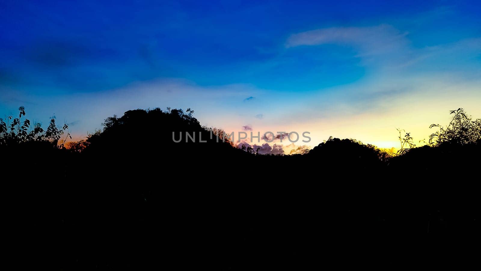 A picturesque silhouette of a landscape set against a vibrant sunset sky, showcasing a blend of blue, orange, and yellow hues. Perfect for themes of nature, tranquility, and beauty.